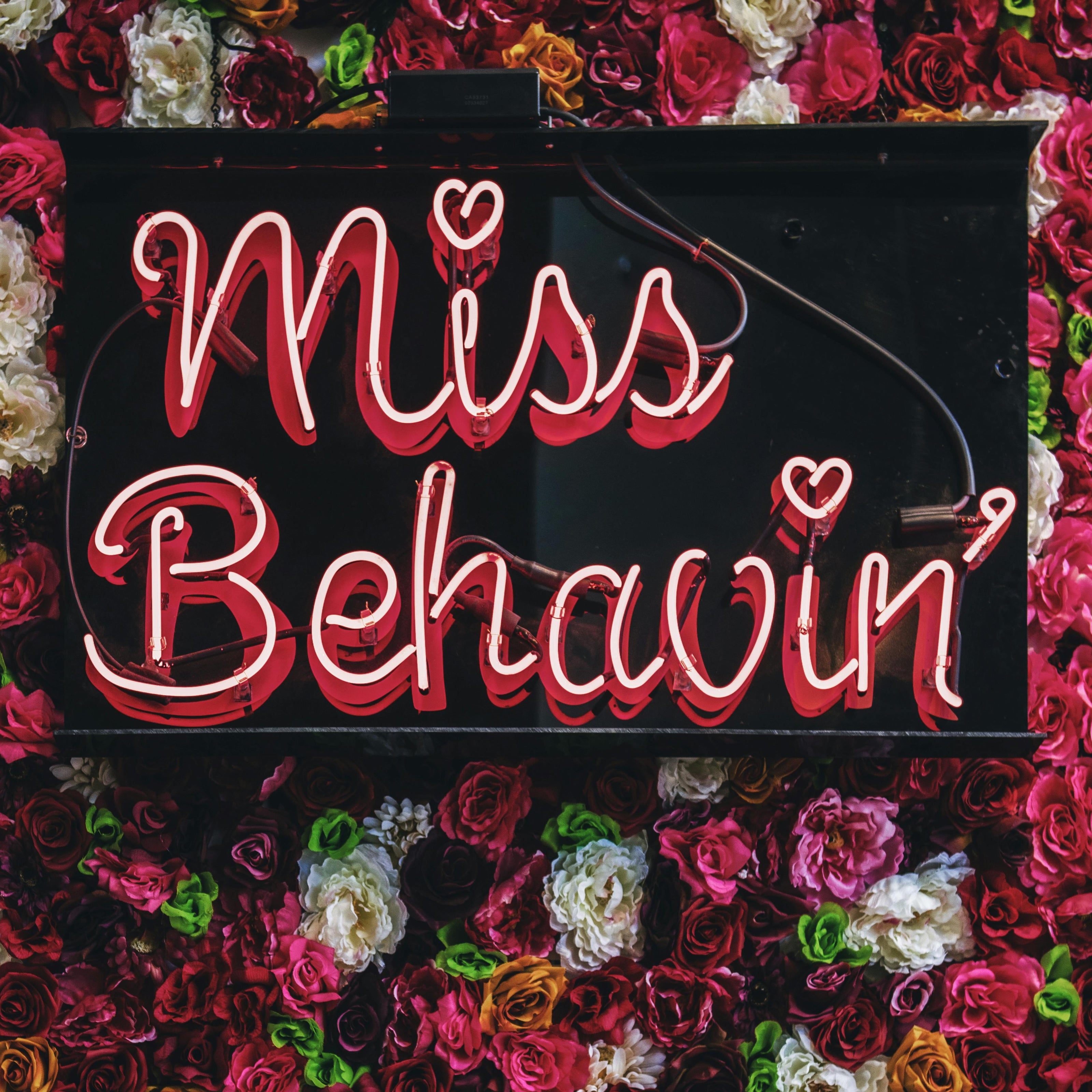 Neon sign with 'Miss Behavin'' surrounded by colorful flowers